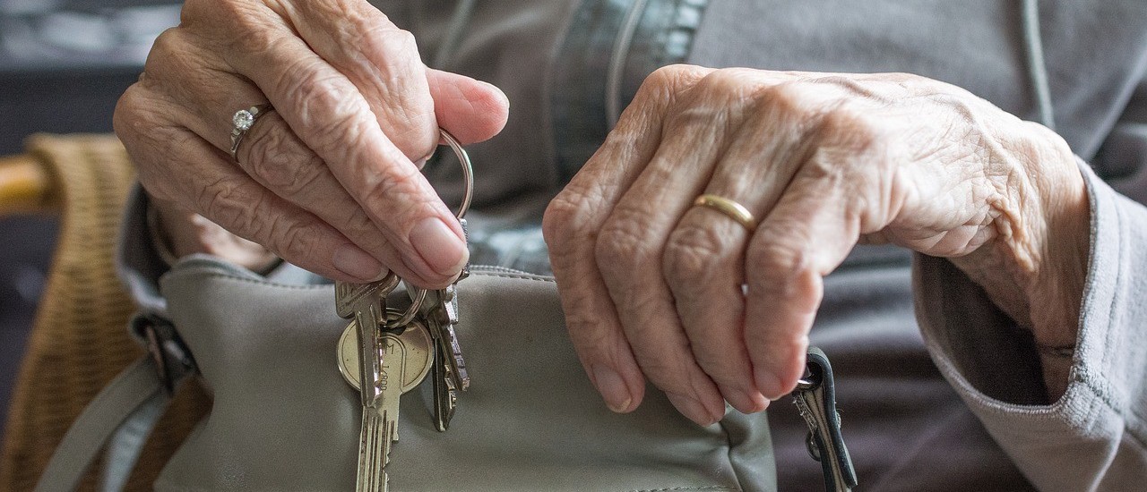 Photo: pixabay The picture shows the hands of an old lady sitting on a chair. She is wearing a diamond ring on her middle finger on her right hand and a gold ring on her ring finder on her left hand. She wears a grey top and puts several keys on a key ring in a grey handbag on her lap.
