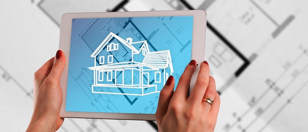 Photo: Pixabay The picture shows the hands of a woman. She is wearing red nail polish and a wide ring on her right ring finger. She is holding a white tablet in her hands on which a sketch of a house can be seen. The screen background is blue and shows the ground plan of a building. The ground plan is also on paper on a table under the tablet. The sketch of the house looks like a projection of the finished building over of the building's ground plan.