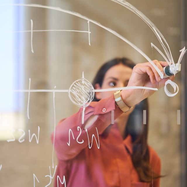 Eine Frau zeichnet eine GGrafik auf eine Glaswand