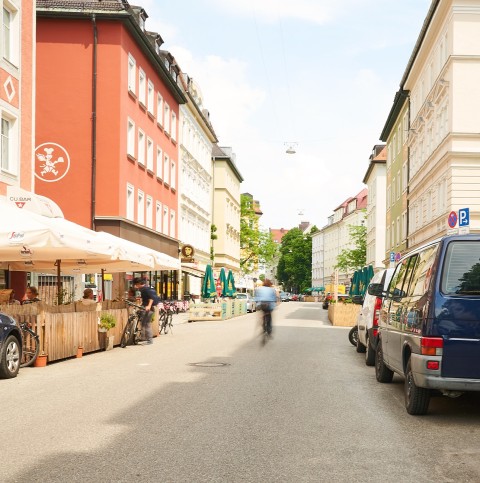 Straße mit Schanigärtern, Radlerin und wenigen Autos