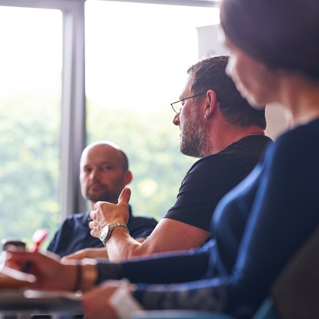 Zwei Männer und eine Frau sitzen nebeneinander, der Mann in der Mitte spricht
