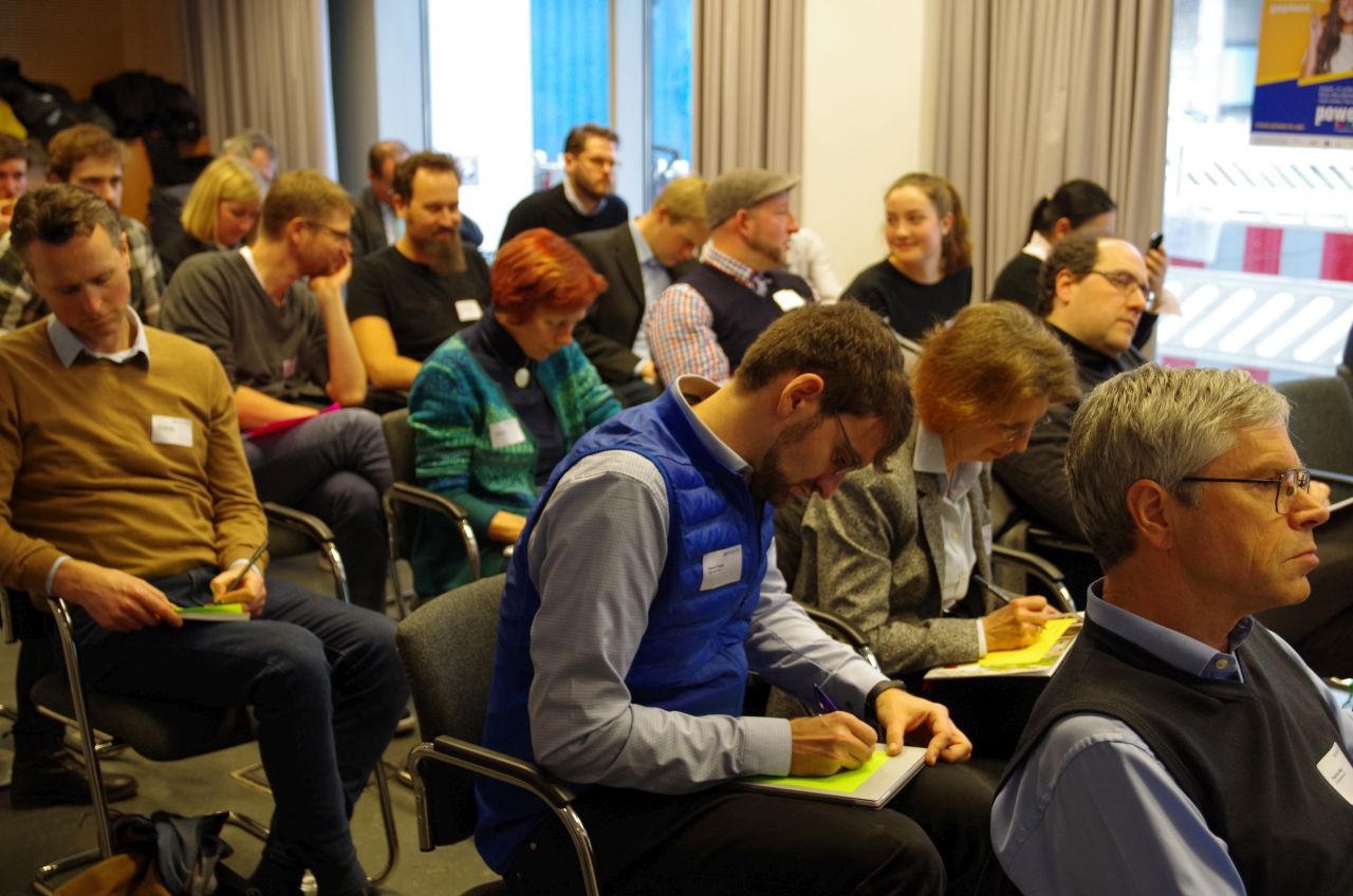 Mehrere Personen sitzen in einem größeren Raum auf Stühlen.