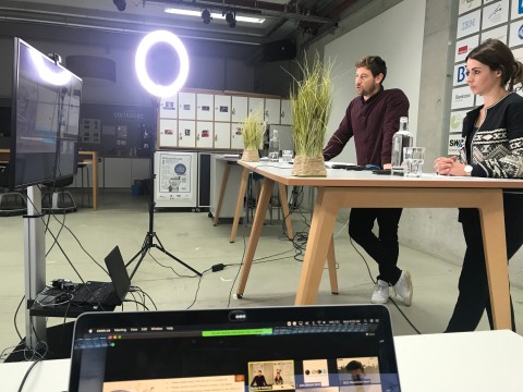 Ein Mann und eine Frau an einem Tisch vor großem Bildschirm