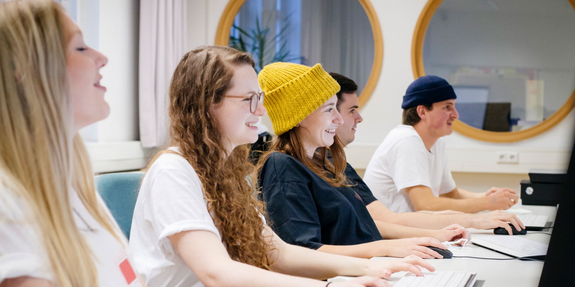 Studierende sitzen in einer Reihe vor Bildschirmen