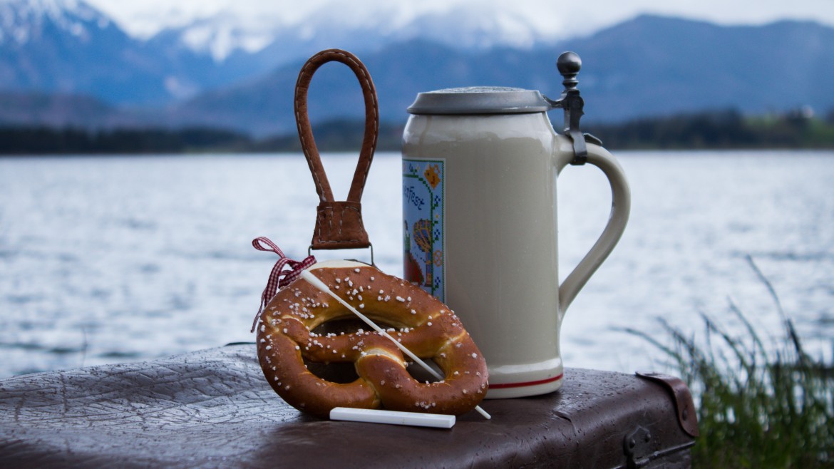 Berg- und Seepanorama mit Bierkrug, Brezel und Coronatest auf einem Reisekoffer