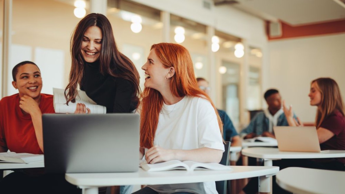 Brunette Frau unterstützt Studierende während der Vorlesung (Jacob Lund Photography, CC BY-NC-ND 2.0 License ) Eine Frau zeigt auf einen Bildschirm auf einem silbernen Rechner und erklärt zwei Studierenden etwas.