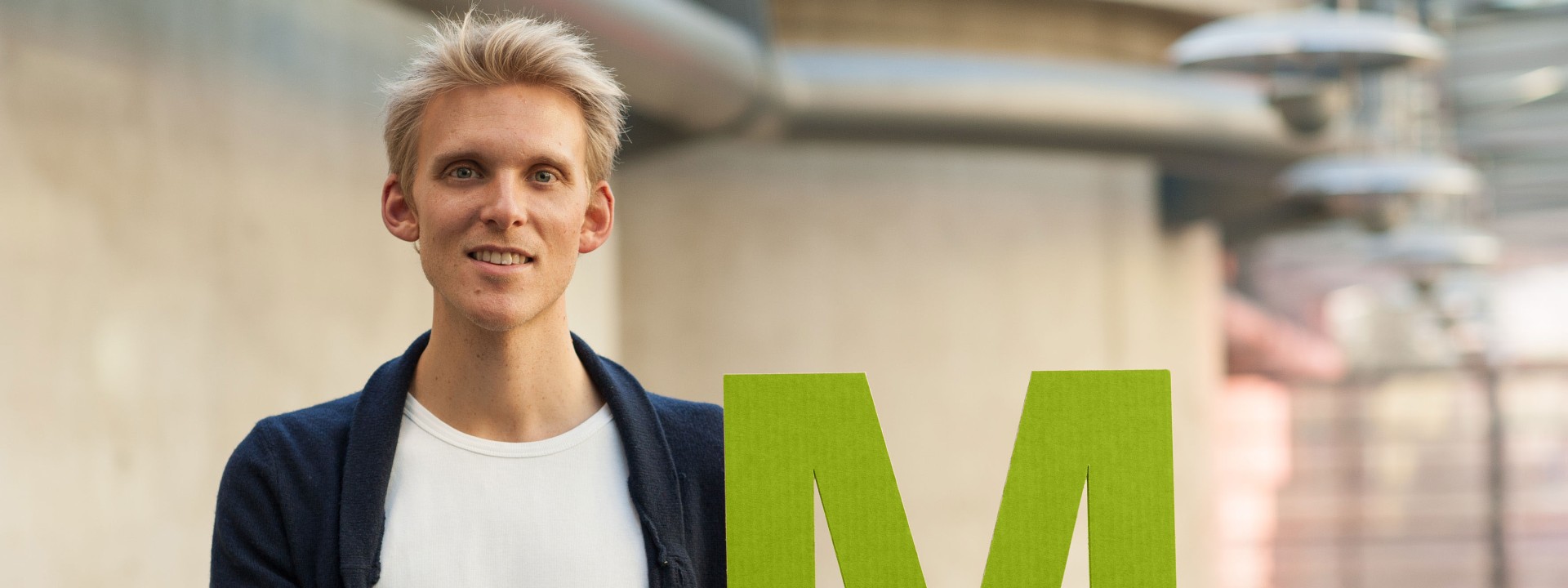 Männliche Person hält ein M für Master vor sich