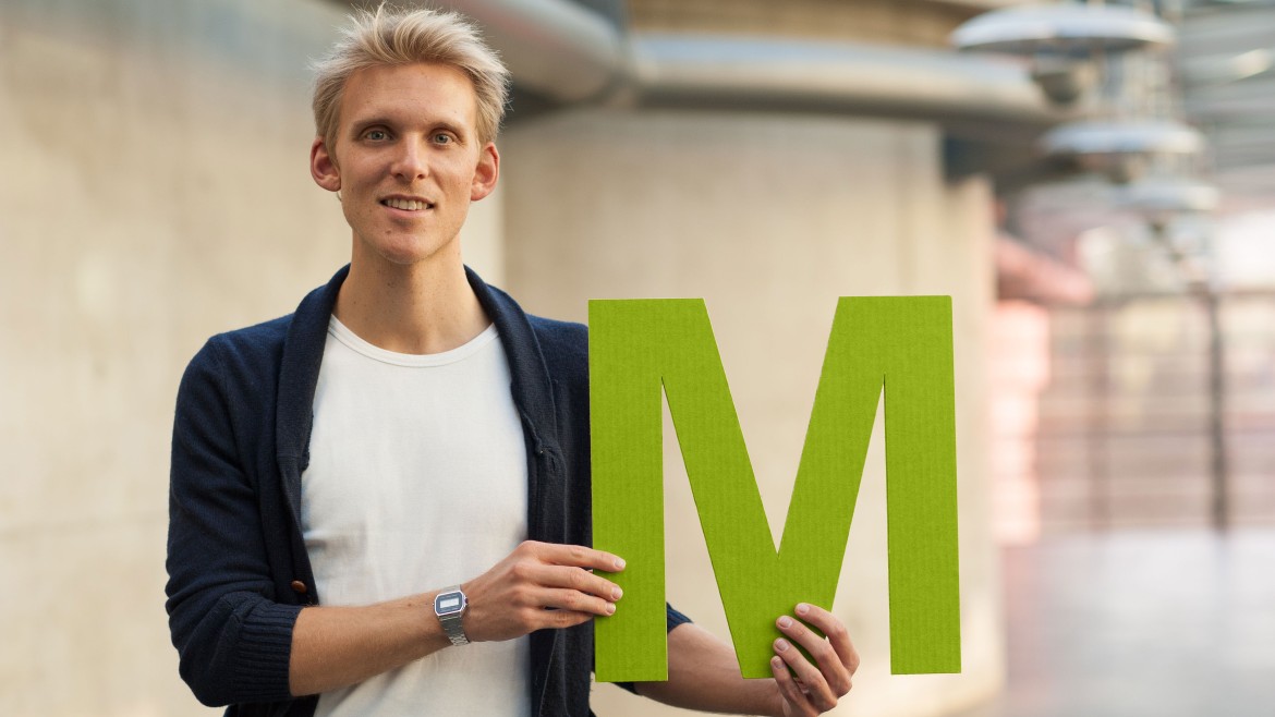 Männliche Person hält ein M für Master vor sich