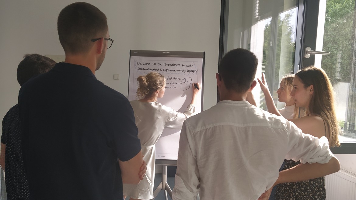 2023_Pers.Fuehrungspot_Flipchart (Foto: Hochschule München) Eine Gruppe Studierender erarbeitet an einem Flipchart Antworten.