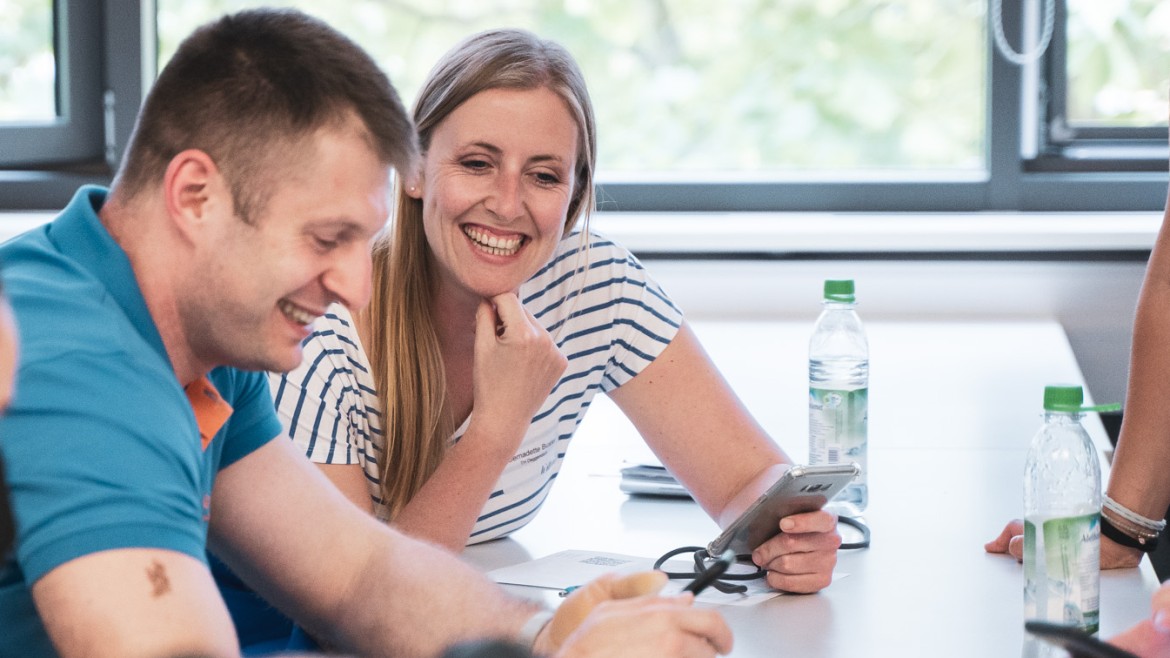 Die HM App - Immer gut informiert! (Foto: Johanna Weber) Mitarbeiter:innen im Gespräch mit Smartphone in der Hand