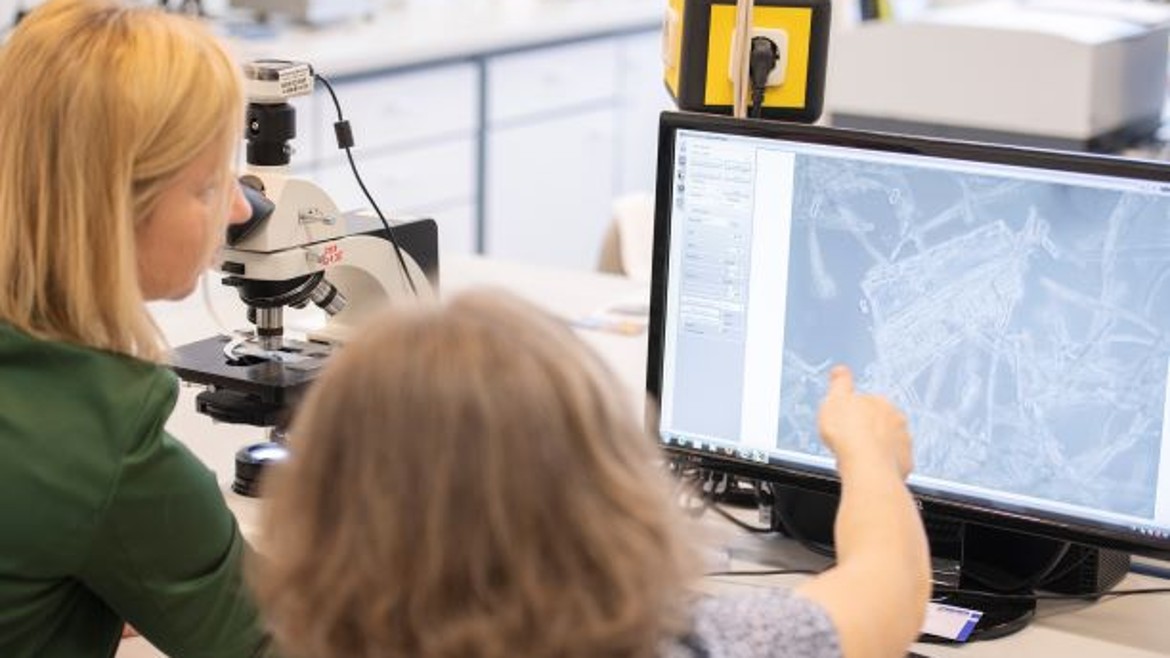 Professorin und Studentin mit Mikroskop und Bildschirm