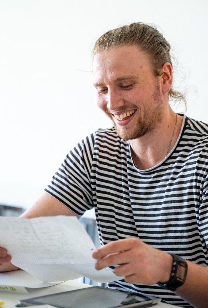 Portrait von Alexander Koppelt, sitzend und lächelnd, während er auf ein Blatt Papier sieht