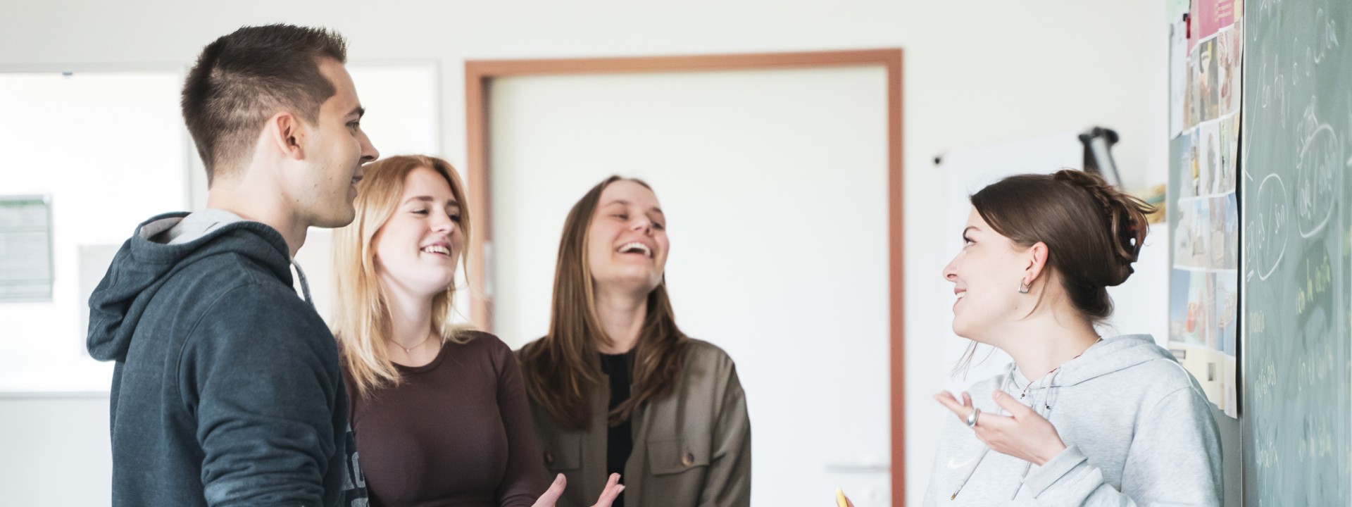 Vier Studierende an Tafel stehend, sprechend und lachend