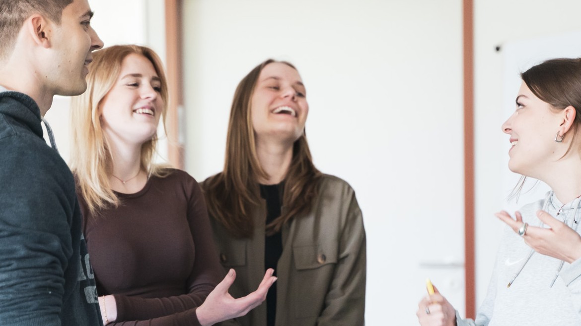 Vier Studierende an Tafel stehend, sprechend und lachend